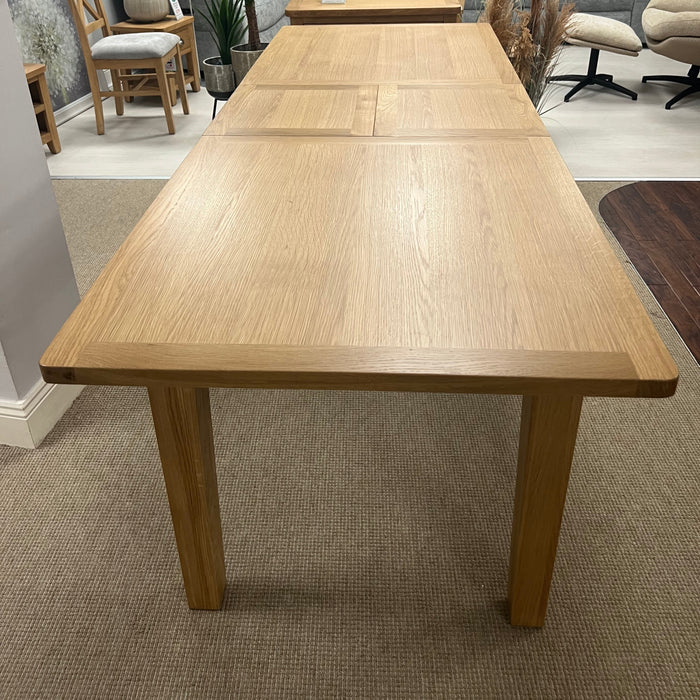 Wooden dining table in a living room setting with gray sofa and decorative items.