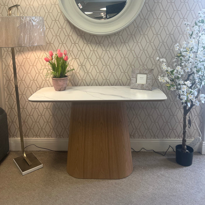The image displays the Athena Console Table in a show room setting, with a wood veneer base and a marble pattern ceramic top, alongside a floor lamp and decorative flowers.